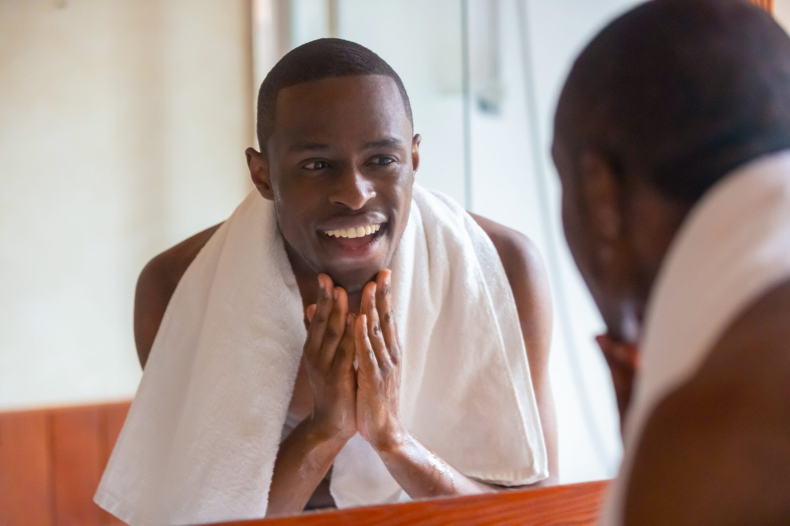 African man looking in mirror cleaning face after shaving Skin + Beard Oil Serum - Image 4